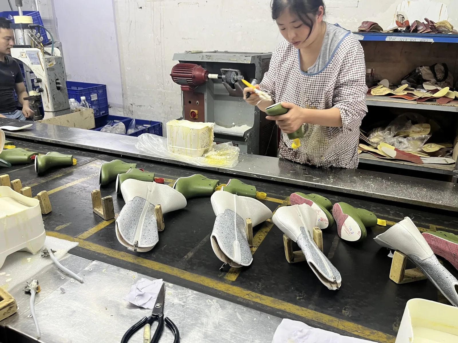 Worker cementing uppers mounted on green shoe lasts on the production line