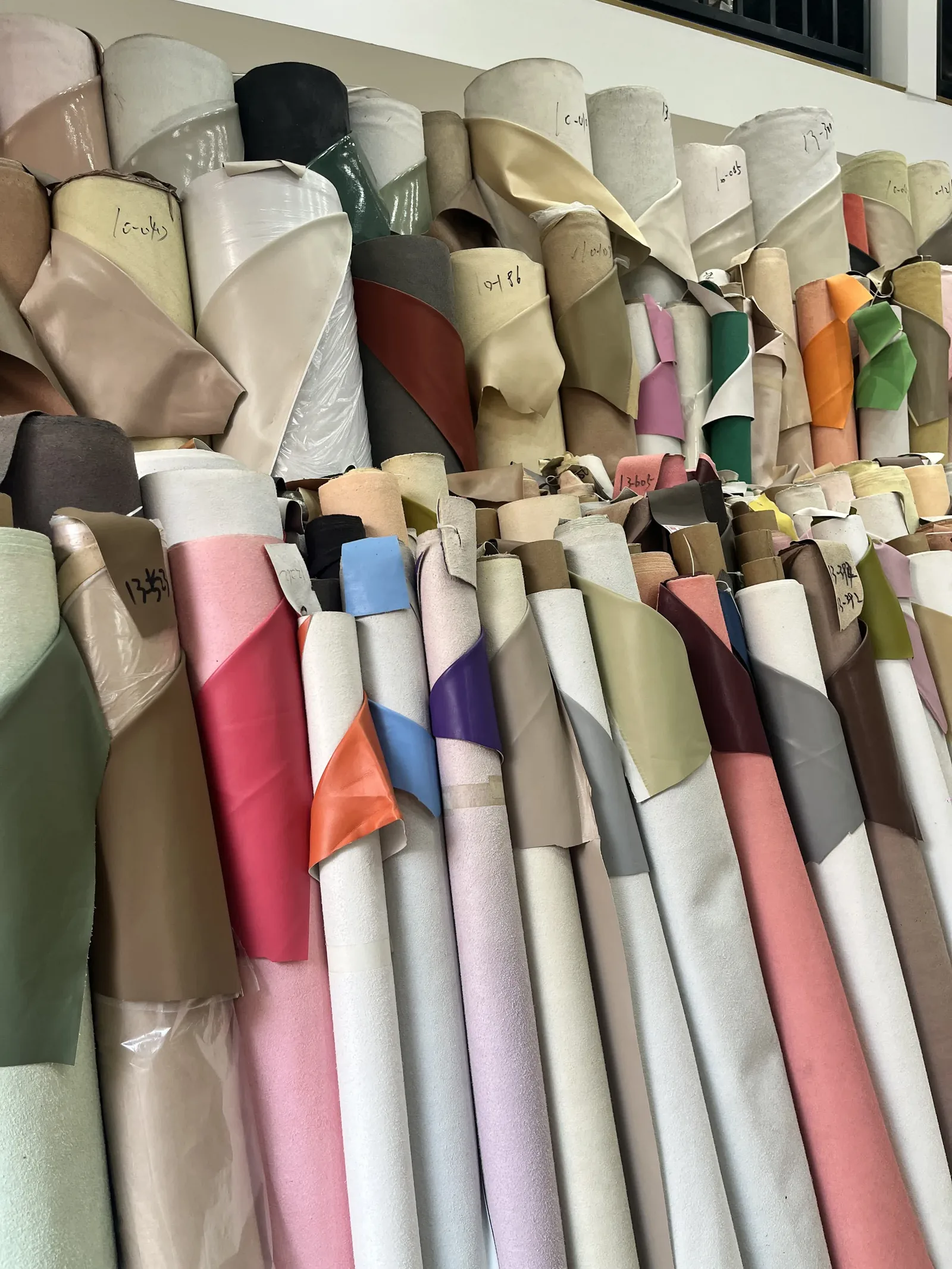 Rolls of leather and materials stacked in a supply warehouse — the materials slice of shoe cost
