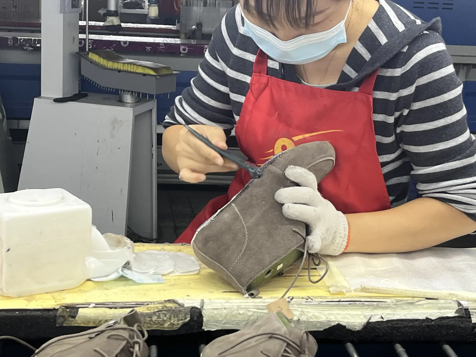 Worker brushing adhesive onto brown shoe uppers before sole bonding — construction detail in quality footwear